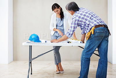 Buy stock photo Attractive young woman with male contractor looking at blueprint for home renovation