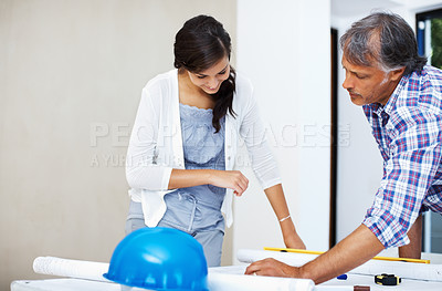 Buy stock photo Beautiful young woman with architect going through blueprint for renovating home