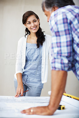 Buy stock photo Smiling young woman discussing home renovation plans with architect over blueprint
