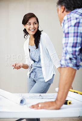 Buy stock photo Beautiful young woman smiling while discussing home renovation plans over blueprint with architect