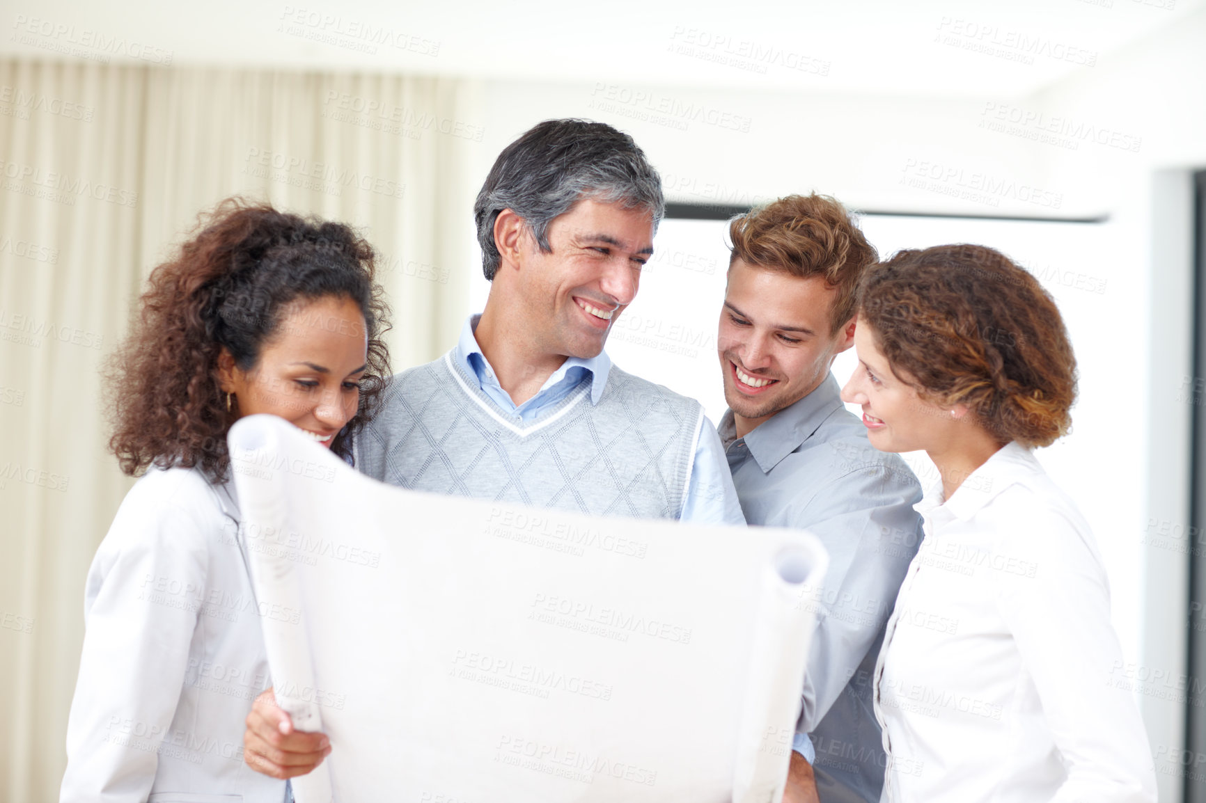 Buy stock photo Shot of a group of four architects looking over blueprints together