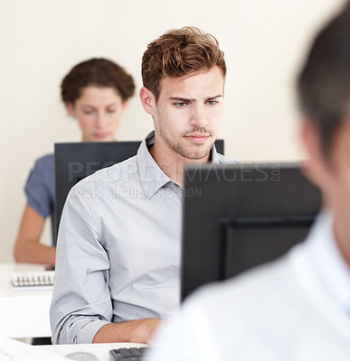 Buy stock photo Shot of a young office worker at work on his computer surrounded by colleagues