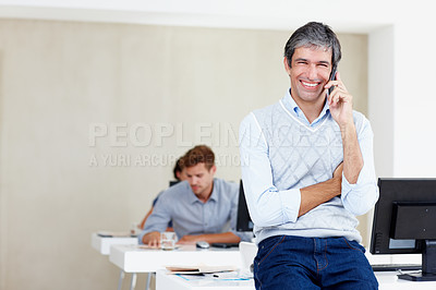 Buy stock photo Portrait of a mature office worker talking on a cellphone with his coworkers sitting behind him