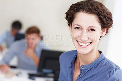 Buy stock photo Portrait of an attractive office worker smiling at the camera with her colleagues working behind her