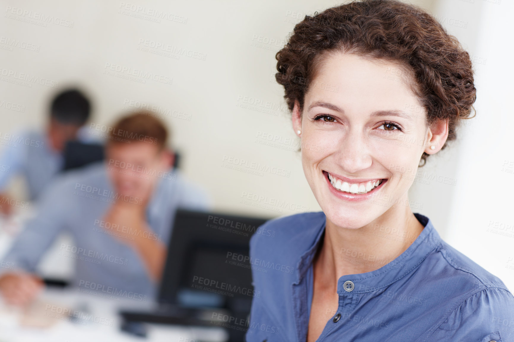 Buy stock photo Portrait of an attractive office worker smiling at the camera with her colleagues working behind her
