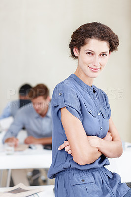 Buy stock photo Portrait of a confident female office worker sitting on her desk with colleagues sitting behind her