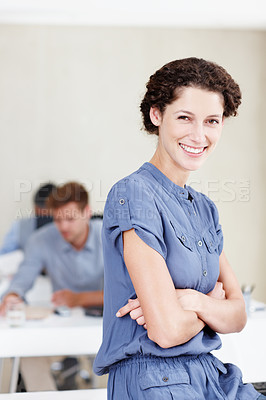 Buy stock photo Portrait of a postive-looking female office worker sitting on her desk with colleagues sitting behind her