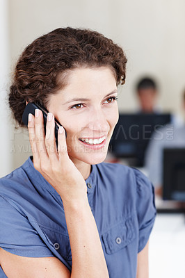 Buy stock photo Shot of a young businesswomen talking on the phone with her coworkers seated behind her