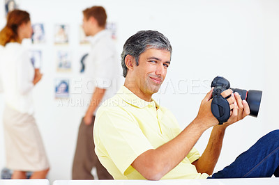 Buy stock photo Portrait of smiling photographer looking at photos in his camera with colleagues in background