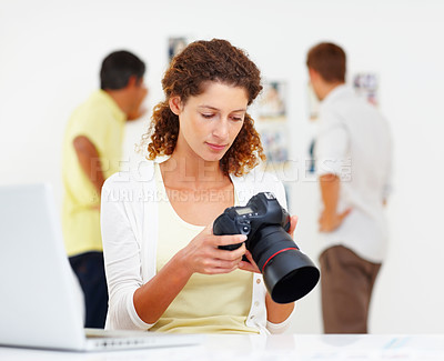 Buy stock photo Female photographer checking out images in camera with colleagues in background