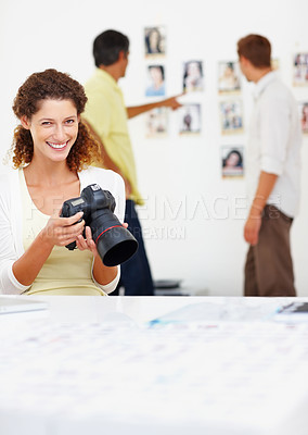 Buy stock photo Portrait of smiling female photographer viewing images in camera with colleagues in background
