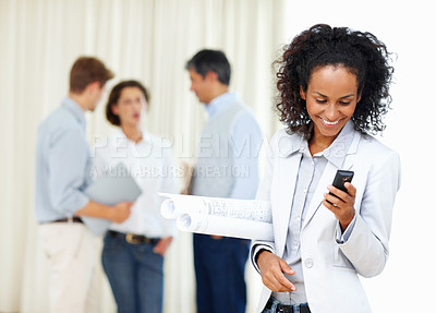 Buy stock photo Young female architect reading text message with colleagues discussing in background