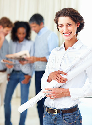 Buy stock photo Beautiful female architect holding blueprints with colleagues discussing in background