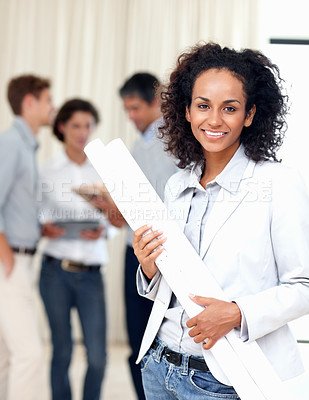 Buy stock photo Beautiful business woman holding blueprints with colleagues discussing in background