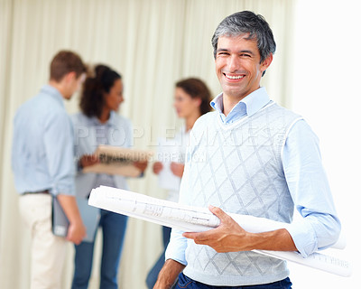 Buy stock photo Portrait of mature business man holding blueprints with colleagues discussing in background