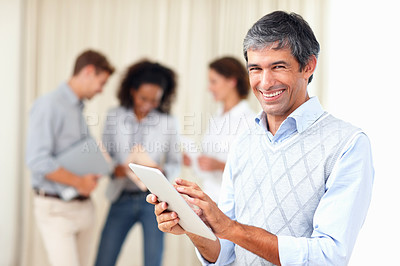Buy stock photo Smiling business man using tablet PC with colleagues discussing in background