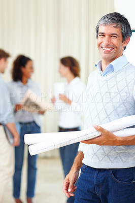 Buy stock photo Mature male architect holding blueprints with colleagues discussing in background