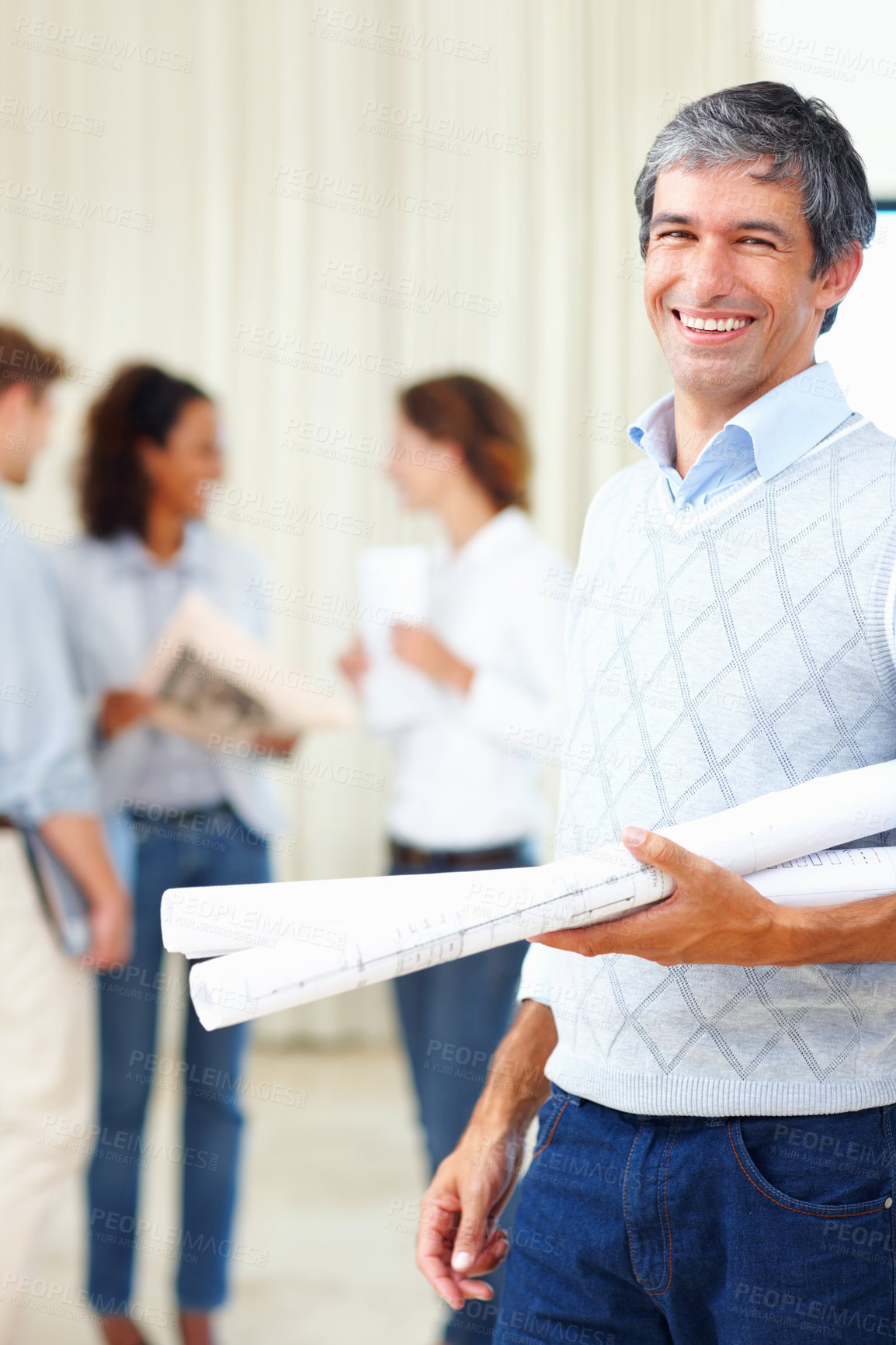 Buy stock photo Mature male architect holding blueprints with colleagues discussing in background
