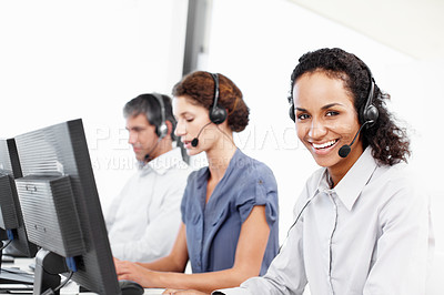 Buy stock photo Portrait of a call center professional working at her computer with colleagues seated in the background