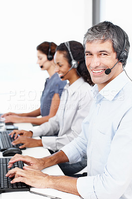 Buy stock photo Portrait of a call center professional working at his computer with colleagues seated in the background