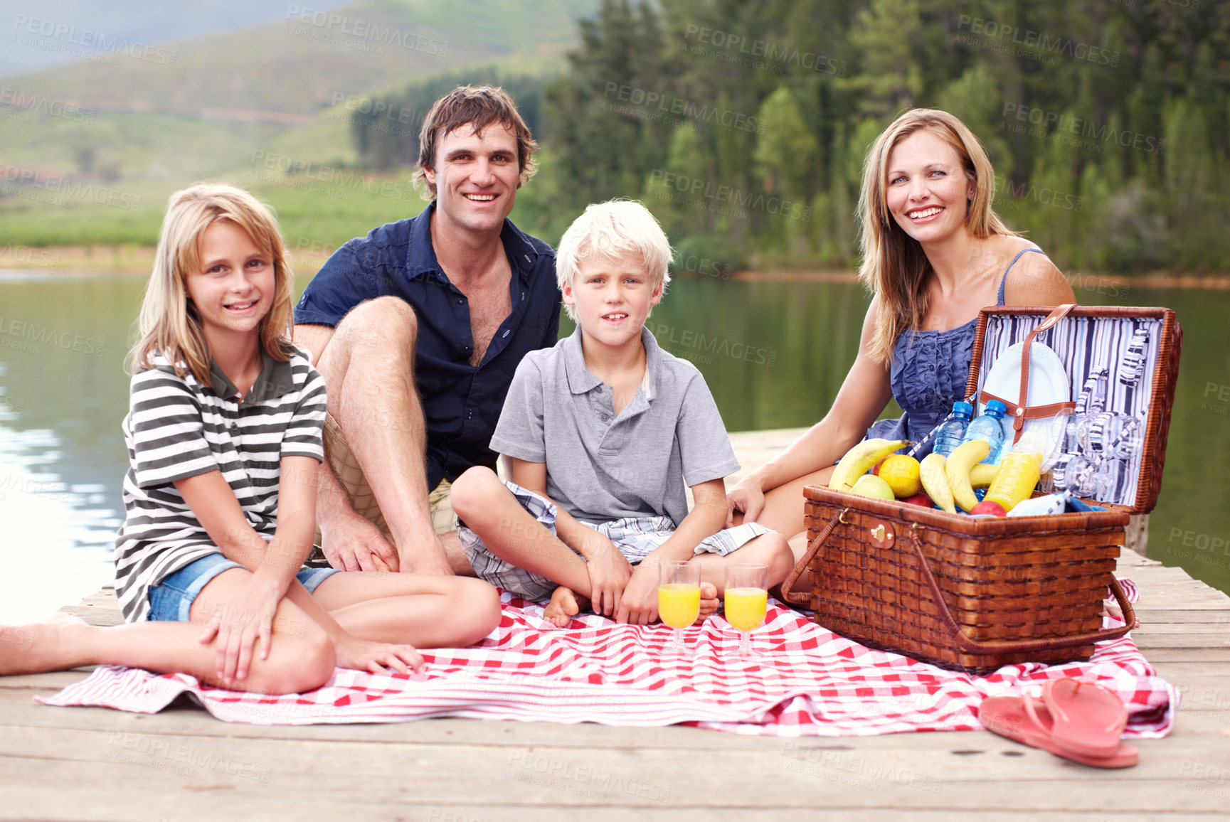 Buy stock photo Family, picnic and portrait by outdoor lake on vacation, countryside bonding and relax on jetty. Parents, kids and food basket for lunch in nature, peace and river for calm security in relationship