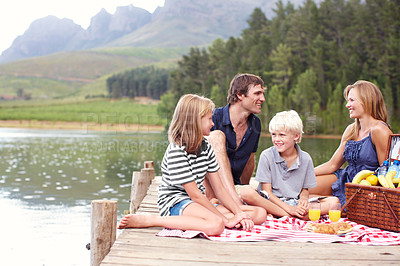 Buy stock photo Happy family, picnic and relax at lake for lunch, celebration or people at thanksgiving on jetty outdoor. Mother, father and kids at river with food on vacation, holiday or bonding by water in summer