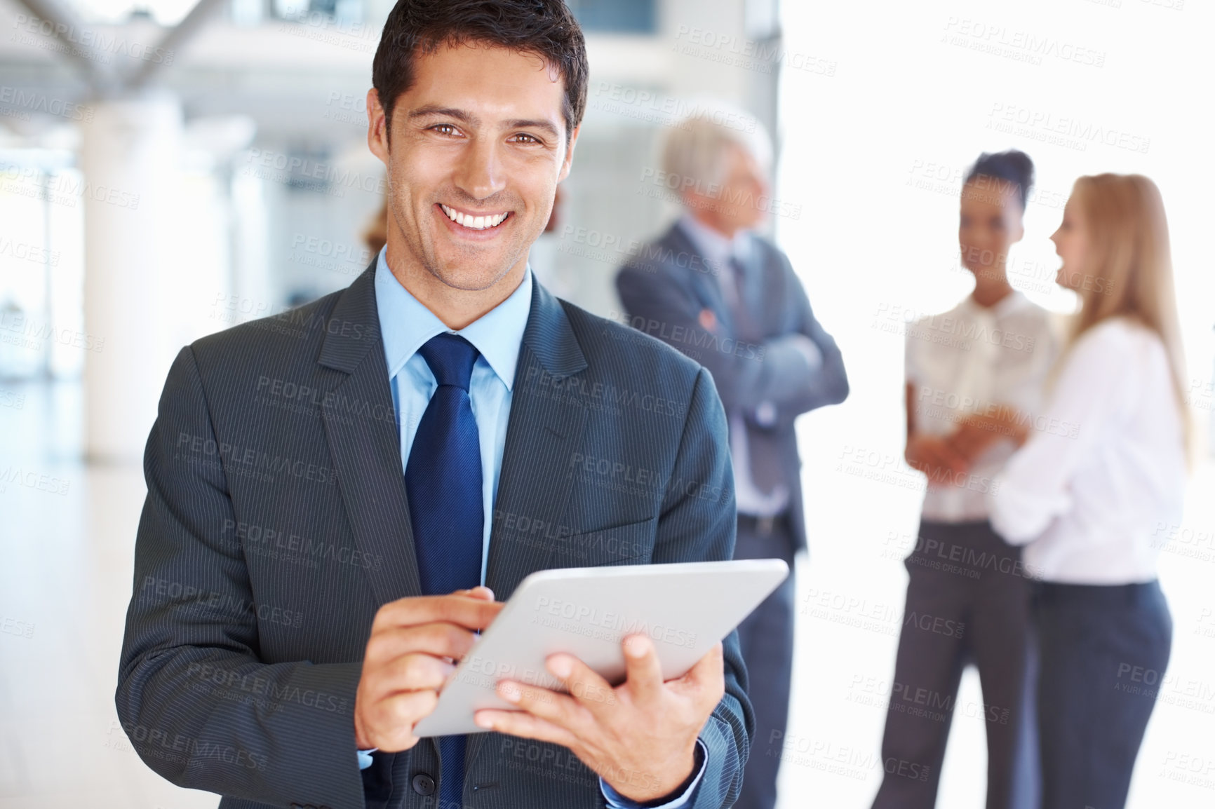 Buy stock photo Portrait of smiling young business man working on digital tablet with executives in background