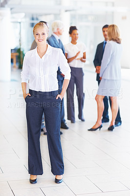 Buy stock photo Full length of young female executive standing with business people discussing in background