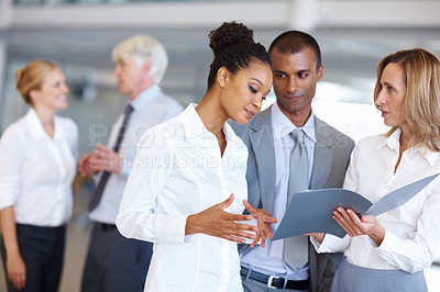 Buy stock photo Portrait of multi racial executives conversing while looking at documents with business people in background