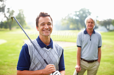 Buy stock photo Portrait of man holding a golf club and smiling with father in background