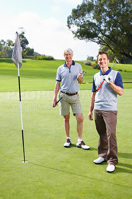 Buy stock photo Full length of father and son standing on the putting green with golf clubs and smiling