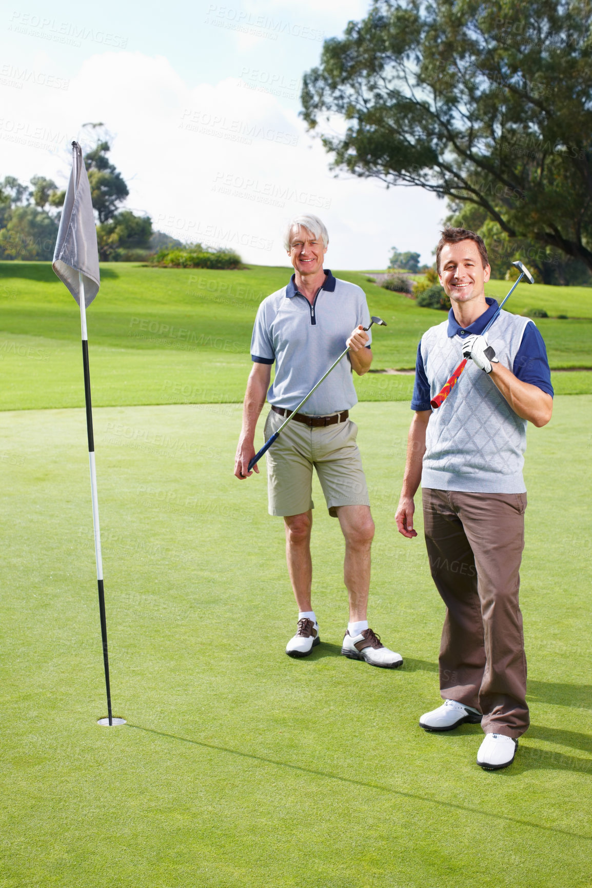 Buy stock photo Full length of father and son standing on the putting green with golf clubs and smiling