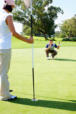 Buy stock photo Couple playing golf with man preparing to putt the ball