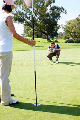 Buy stock photo Couple playing golf with man preparing to putt the ball and woman holding the flagstick