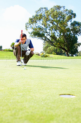Buy stock photo Full length of crouched male golfer on the putting green lining up the putt