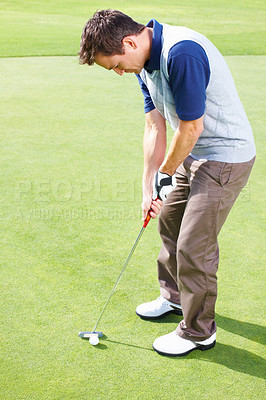 Buy stock photo Male golfer standing on the putting green and taking his position to putt the ball