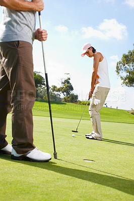 Buy stock photo Young woman putting on the golf course with her husband in the background