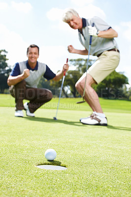 Buy stock photo Two excited men on the green during a round of golf watching the ball rolling into the hole
