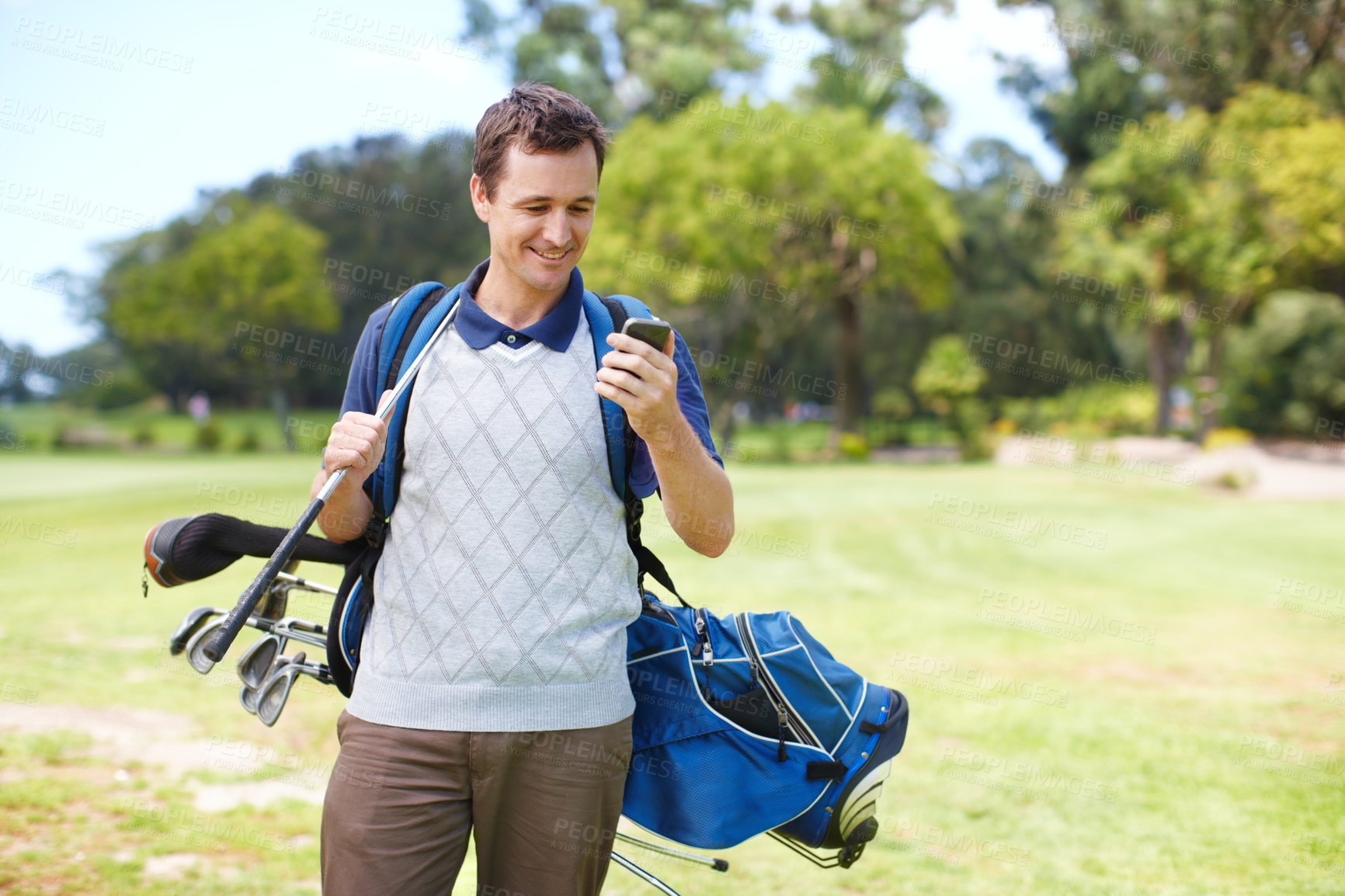 Buy stock photo Smiling golfer using his mobile on the course while carrying his clubs