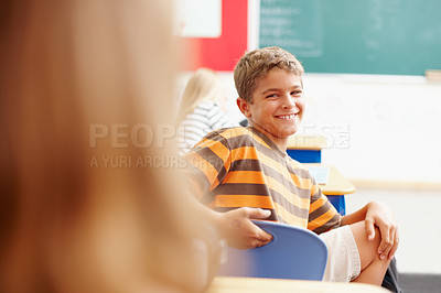 Buy stock photo Smiling young boy turning round in class to look at a classmate - copyspace