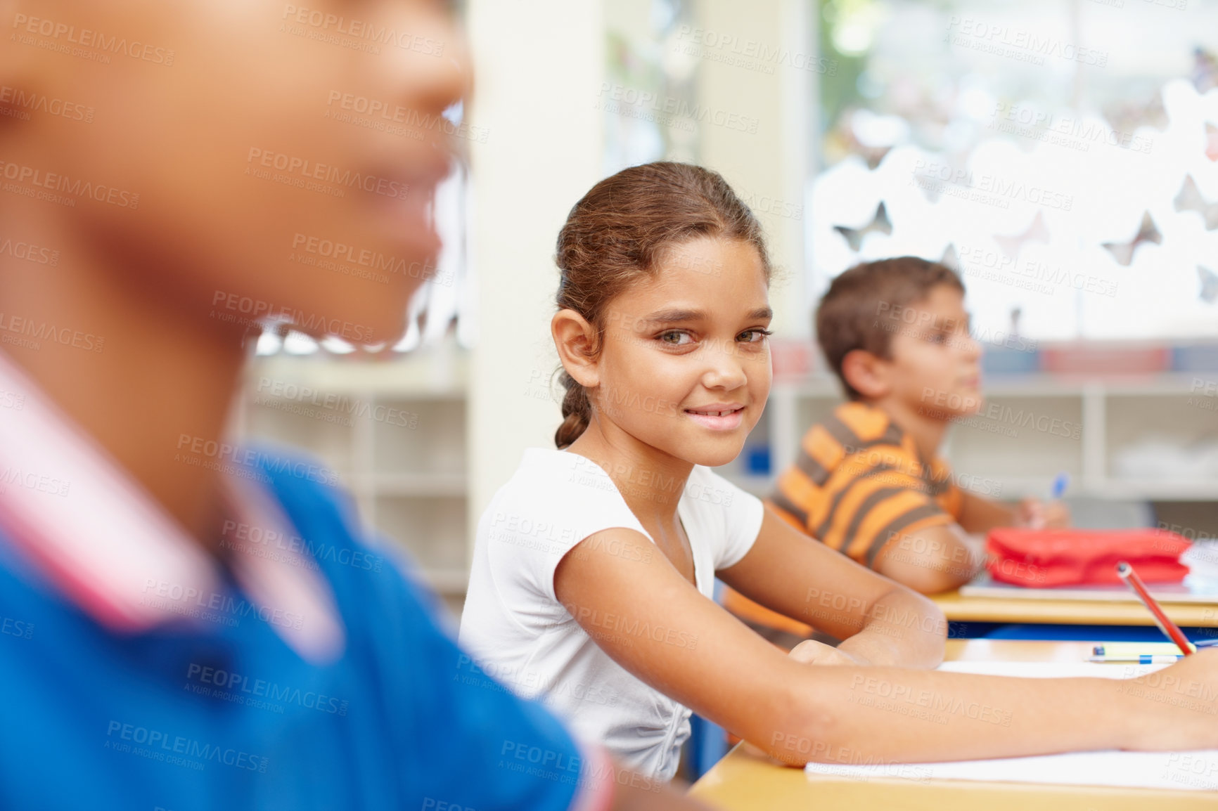 Buy stock photo Smile, portrait and girl in kids classroom for writing test, growth and child development at elementary school. Happy, face and student at desk for education, study and assessment for scholarship.