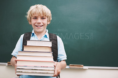 Buy stock photo A cute young boy carrying a stack of books against a blackboard in the classroom