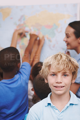Buy stock photo A young boy standing in the classroom as his friends and teacher look over a world map