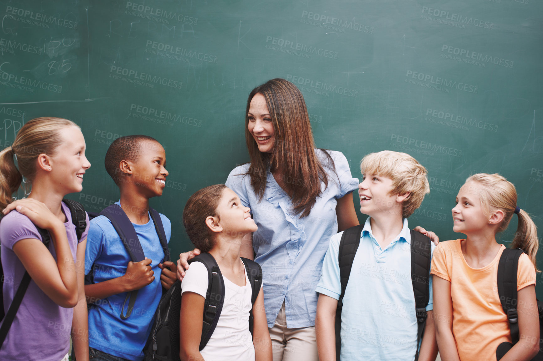 Buy stock photo A pretty young teacher standing with her classroom at the blackboard and smiling