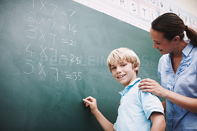 Buy stock photo A pretty teacher standing at the blackboard with a young student and helping him with his maths