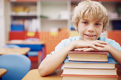 Buy stock photo A happy young boy sitting at his desk and leaning his chin on a stack of books