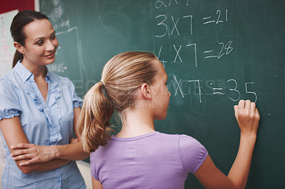 Buy stock photo A pretty young teacher helping her student with a maths problem at the blackboard