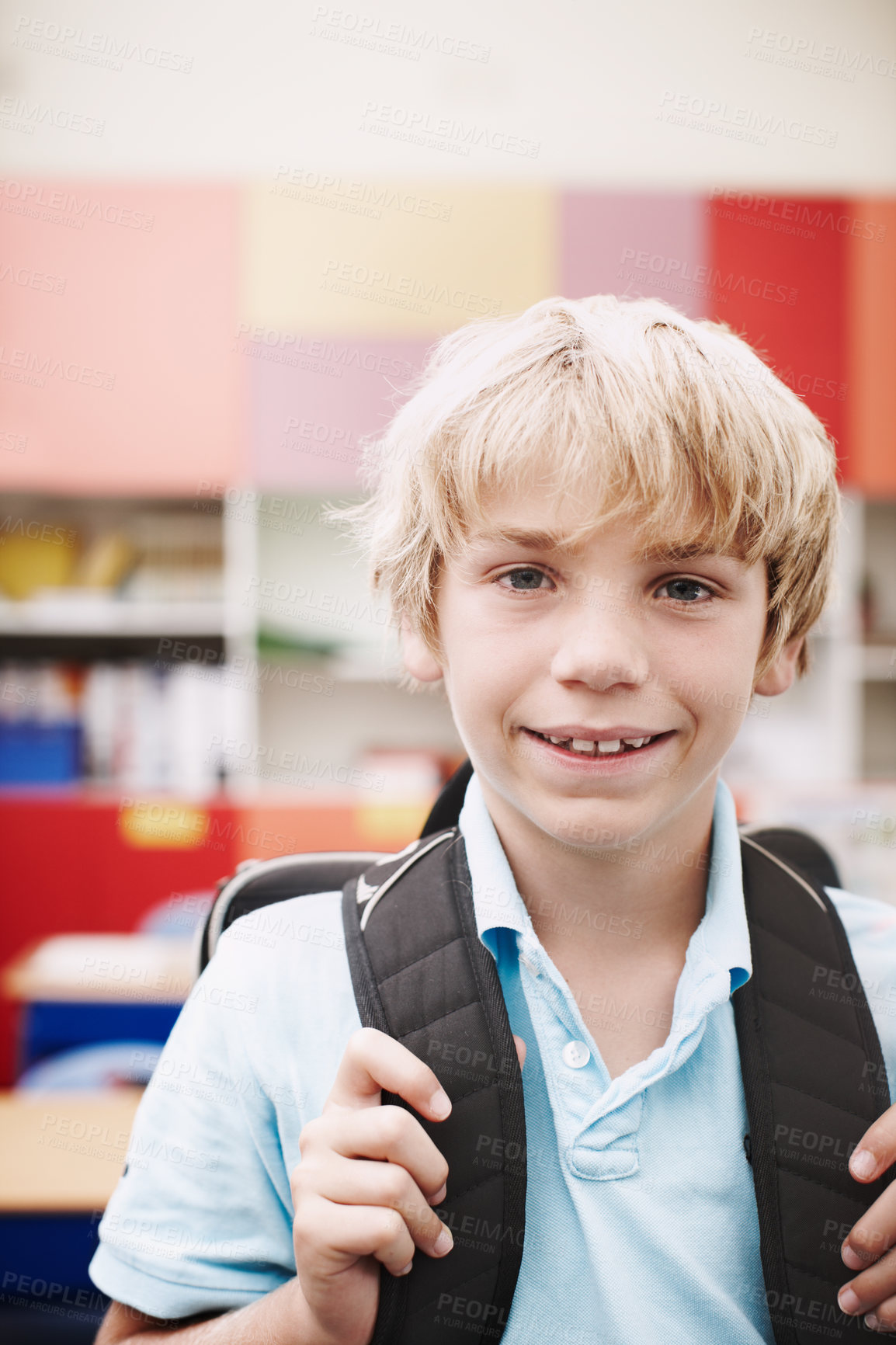 Buy stock photo A young boy holding the straps of his backpack and standing in his classroom