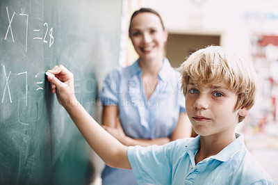 Buy stock photo A young boy doing mathematics on the blackboard as his teacher watches with a smile