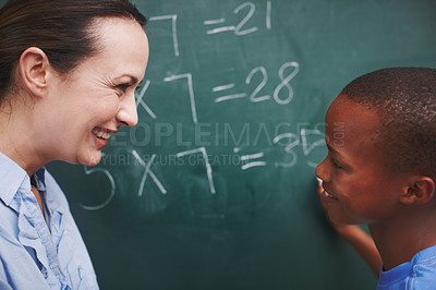 Buy stock photo A young boy and his teacher looking at each other while he does sums on the board